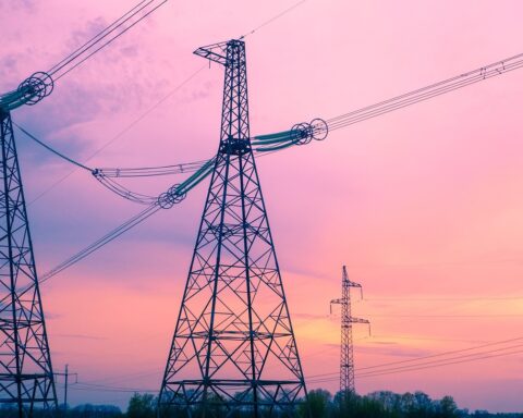 Some electric distribution towers stand amidst a pinkish, blue sunset.