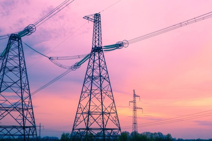 Some electric distribution towers stand amidst a pinkish, blue sunset.