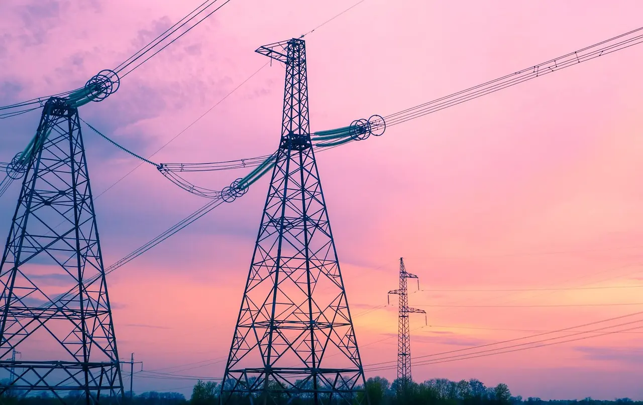 Some electric distribution towers stand amidst a pinkish, blue sunset.