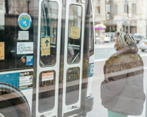 Masked lady waits for bus door to open.