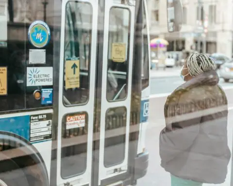 Masked lady waits for bus door to open.