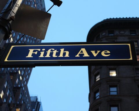 A Fifth Avenue sign in New York City is imposed on a blue sky.