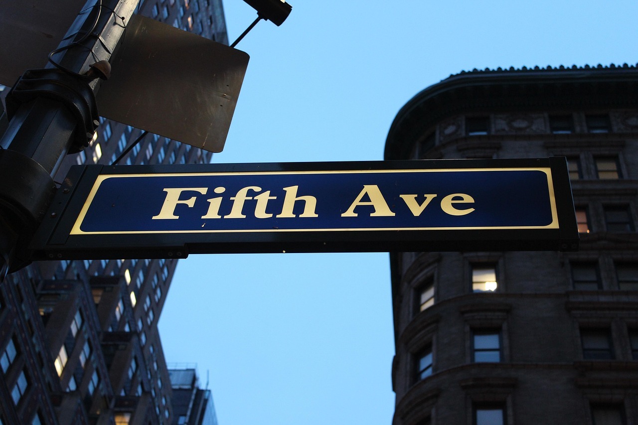 A Fifth Avenue sign in New York City is imposed on a blue sky.