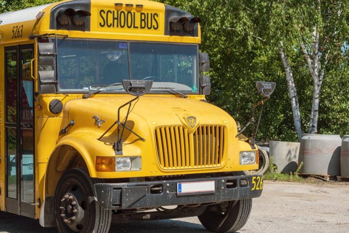 A school bus sits on an empty street with trees along the road beside.