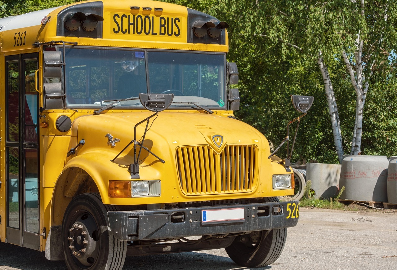 A school bus sits on an empty street with trees along the road beside.