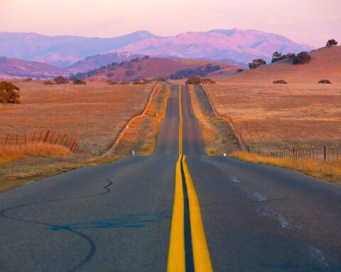 A one lane road is illuminated by a sunset over the mountains.