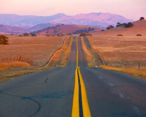 A one lane road is illuminated by a sunset over the mountains.