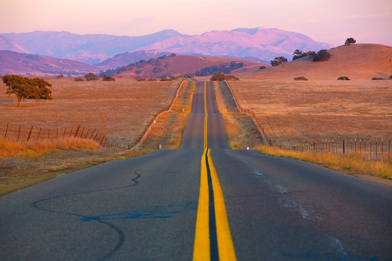 A one lane road is illuminated by a sunset over the mountains.