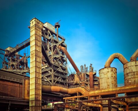 A rusty industrial building sits untouched amid a blue sky.
