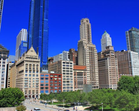 The Chicago skyline shines in the daylight with a clear blue sky in the background.