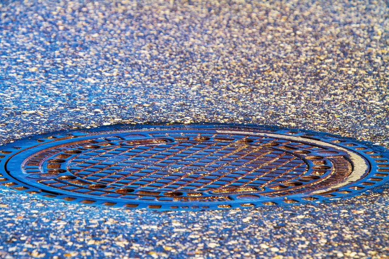 A sewer cover is photographed in the middle of a street.