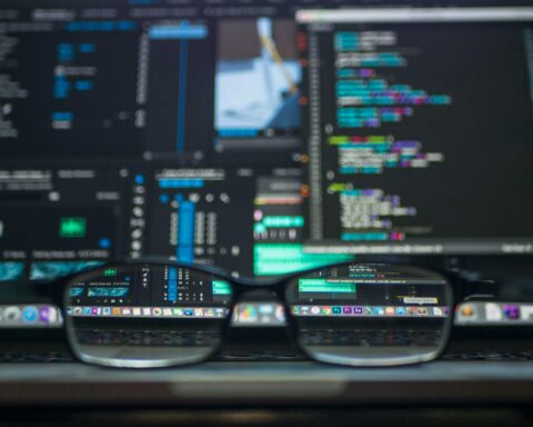 A pair of glasses is in front of a computer screen with various codes and programs.