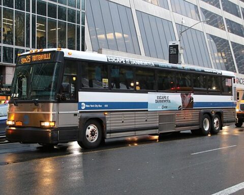 A silver bus with advertisements waits on a busy road during traffic.