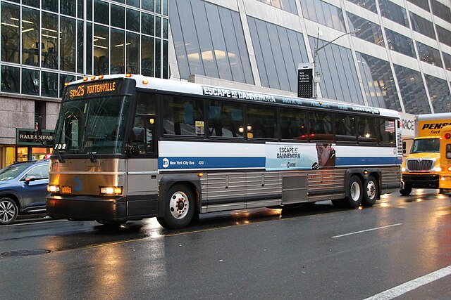 A silver bus with advertisements waits on a busy road during traffic.