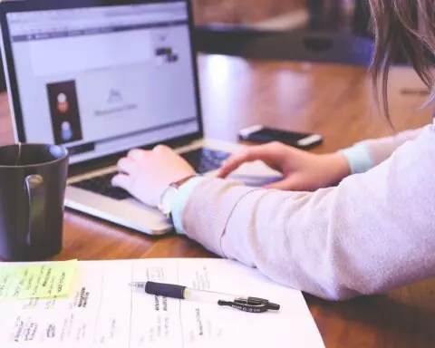 woman's arms operating a laptop computer with notes on the desk