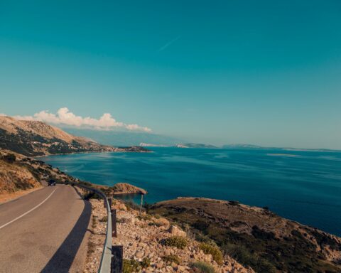 a road curves around a coastline with blue skies