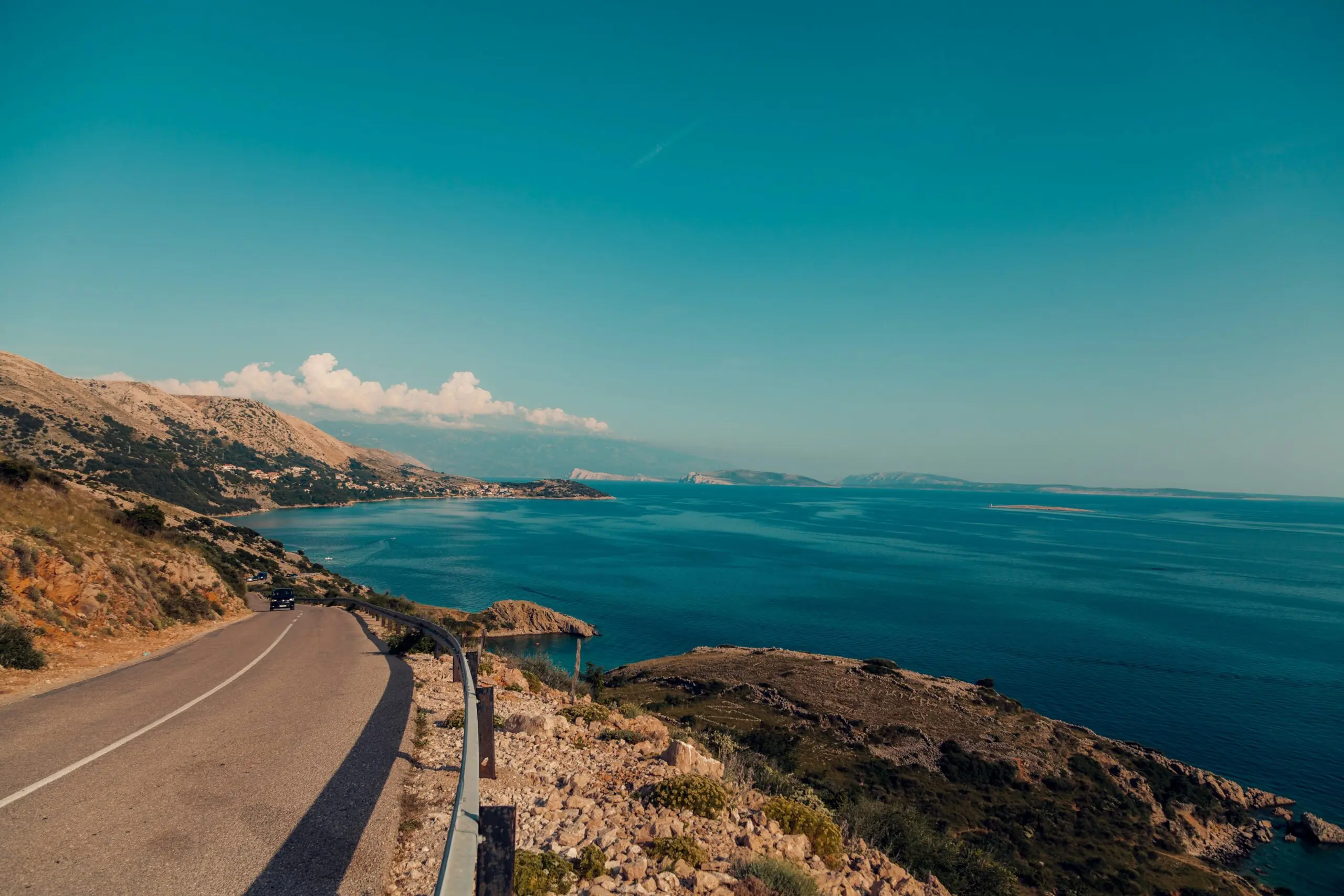 a road curves around a coastline with blue skies