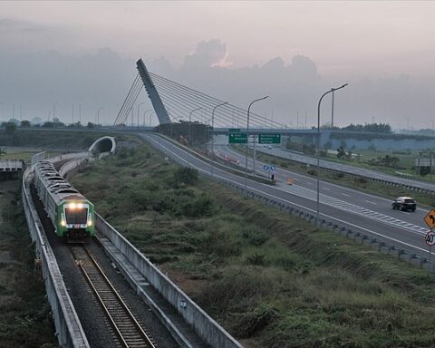 an aerial view shows a roll road parallel to a train coming down tracks in front of a cloudy sky