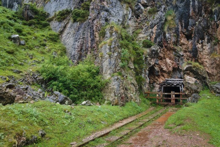 An abandoned mine shaft sits at the bottom of a rocky mountain cliff.