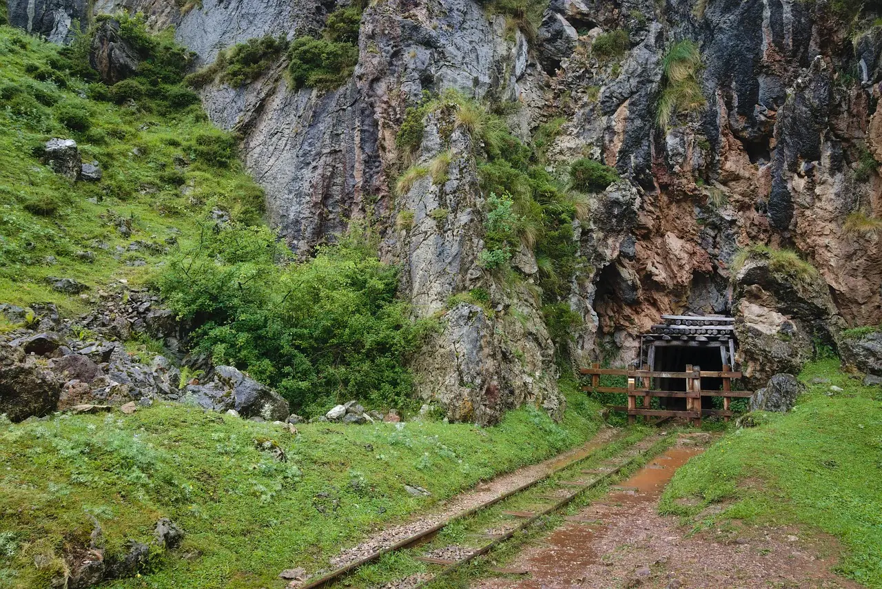 An abandoned mine shaft sits at the bottom of a rocky mountain cliff.