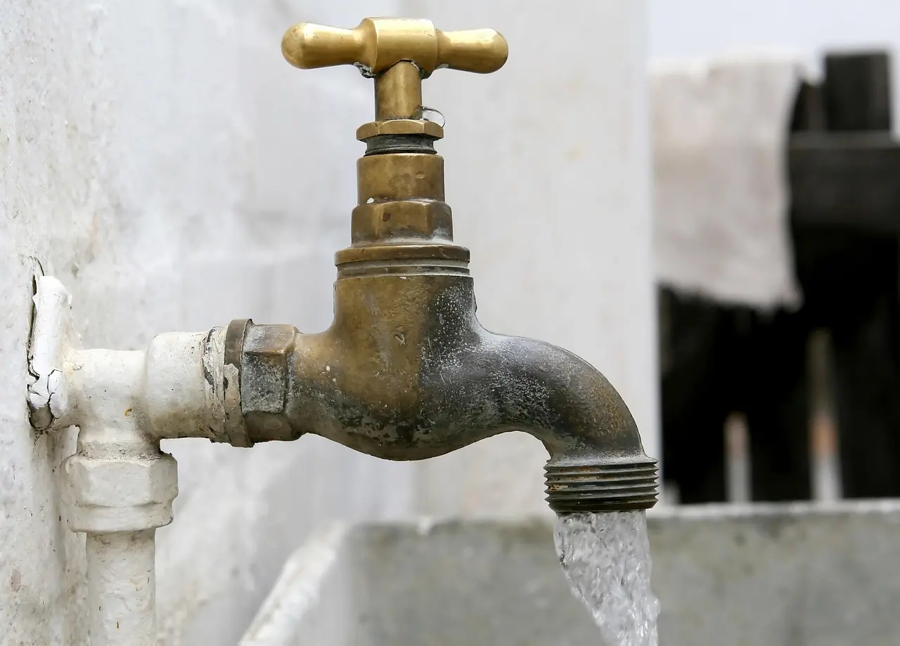An outdoor faucet pours a stream of water into an attached sink.