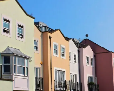 A row of vibrantly colored multi-family homes is illuminated by sunshine and a blue sky.