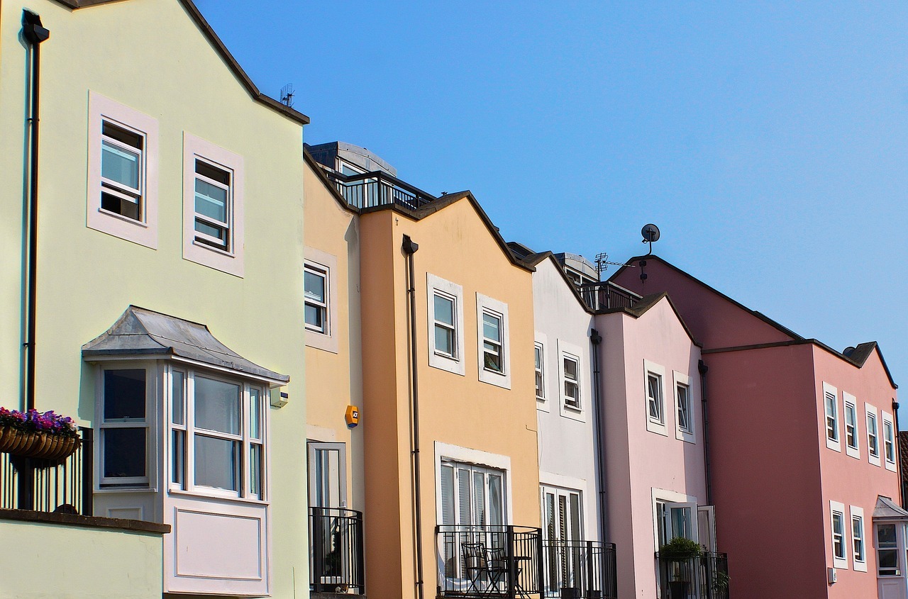 A row of vibrantly colored multi-family homes is illuminated by sunshine and a blue sky.