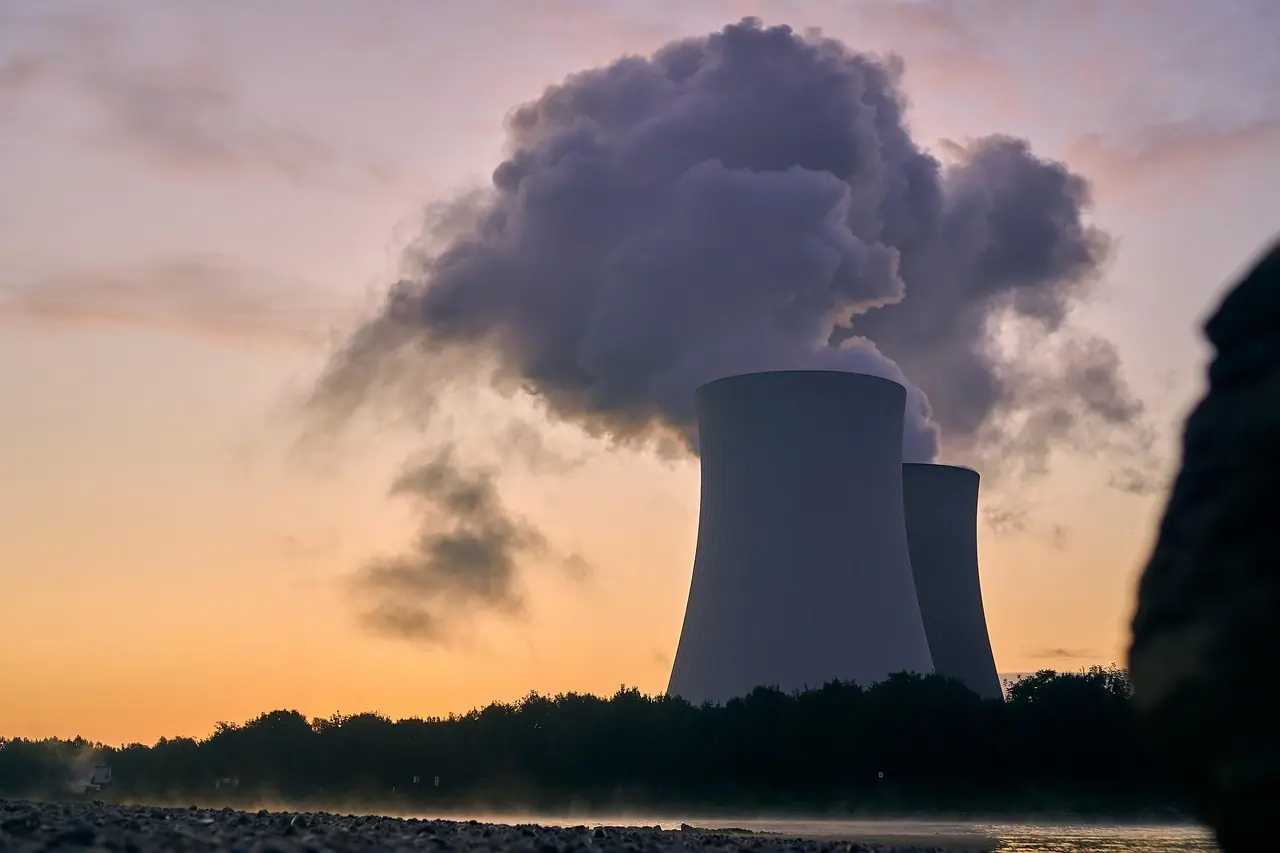 The image depicts a nuclear reactor in operations in front of a setting sun.