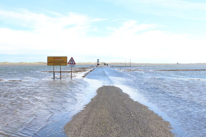 A sign notifies drivers of the potential of a washed out or flooded road as the road below is partially submerged in water.