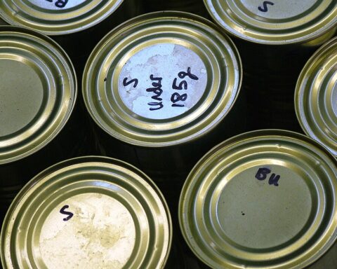 The photo depicts the tops of seven cans with various writing on some of the cans.