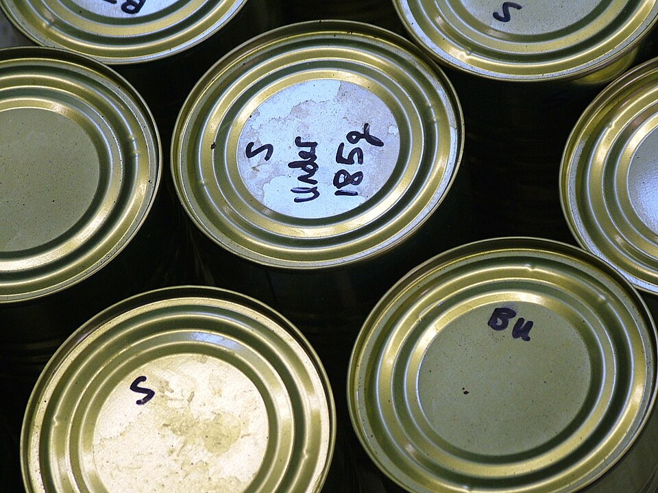 The photo depicts the tops of seven cans with various writing on some of the cans.