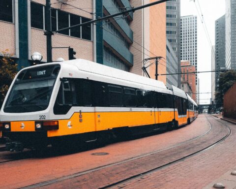 A yellow and white tram in Dallas curves through a building-congested corridor.