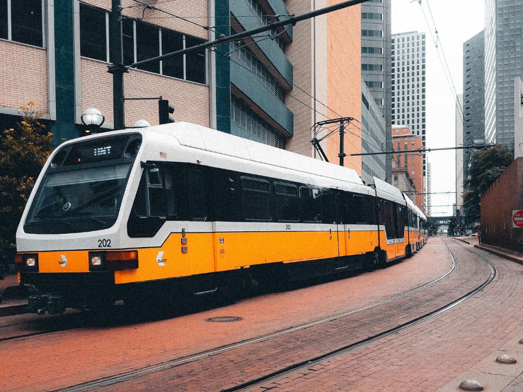 A yellow and white tram in Dallas curves through a building-congested corridor.