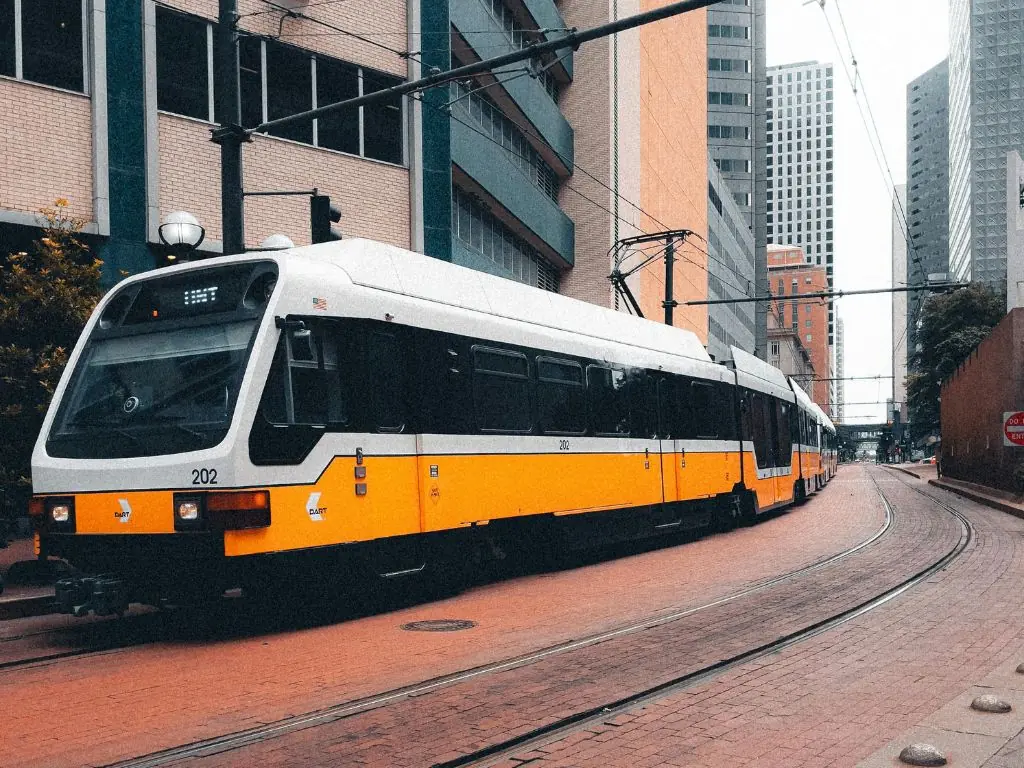 A yellow and white tram in Dallas curves through a building-congested corridor.