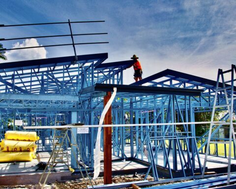 Construction workers work on a housing development held up by blue structuring.