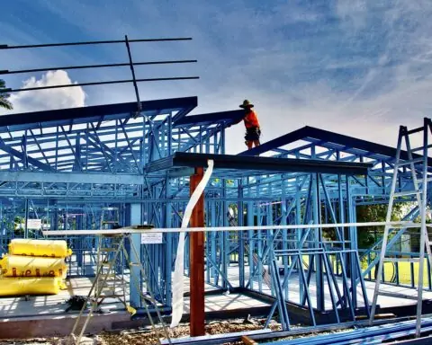 Construction workers work on a housing development held up by blue structuring.