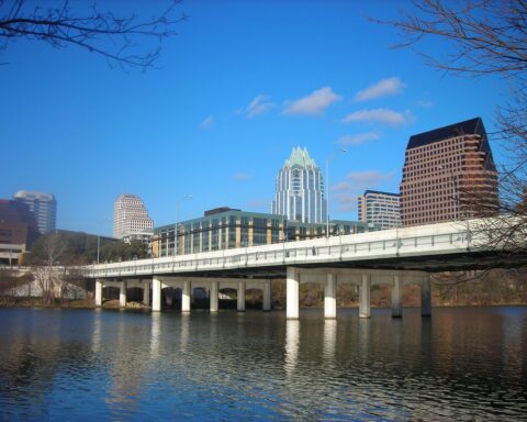 A bridge, backlit by large skyscrappers, casts over the Lady Bird Lake in Austin, Texas.