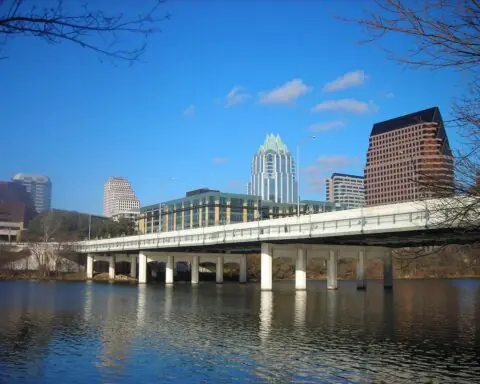 A bridge, backlit by large skyscrappers, casts over the Lady Bird Lake in Austin, Texas.