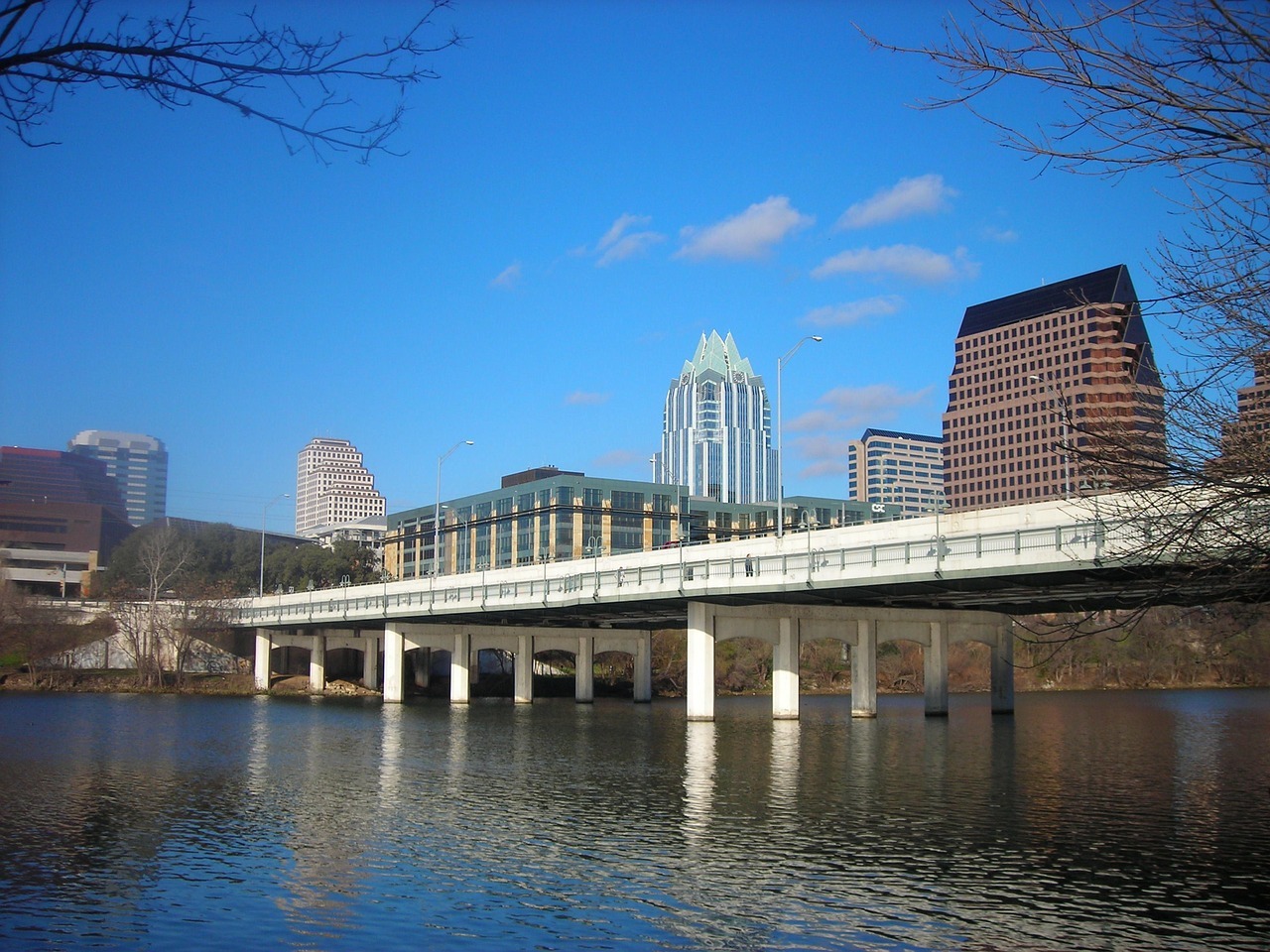 A bridge, backlit by large skyscrappers, casts over the Lady Bird Lake in Austin, Texas.