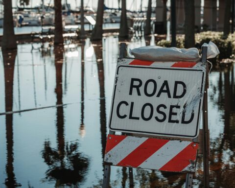 A road closed sign next to a flooded road.