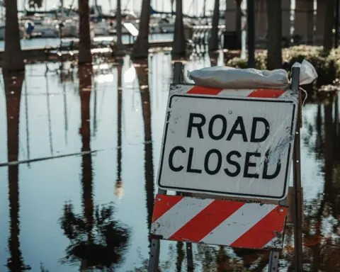 A road closed sign next to a flooded road.