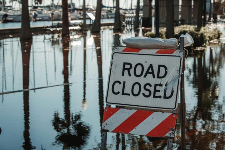 A road closed sign next to a flooded road.