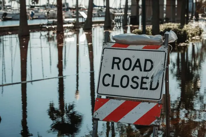 A road closed sign next to a flooded road.