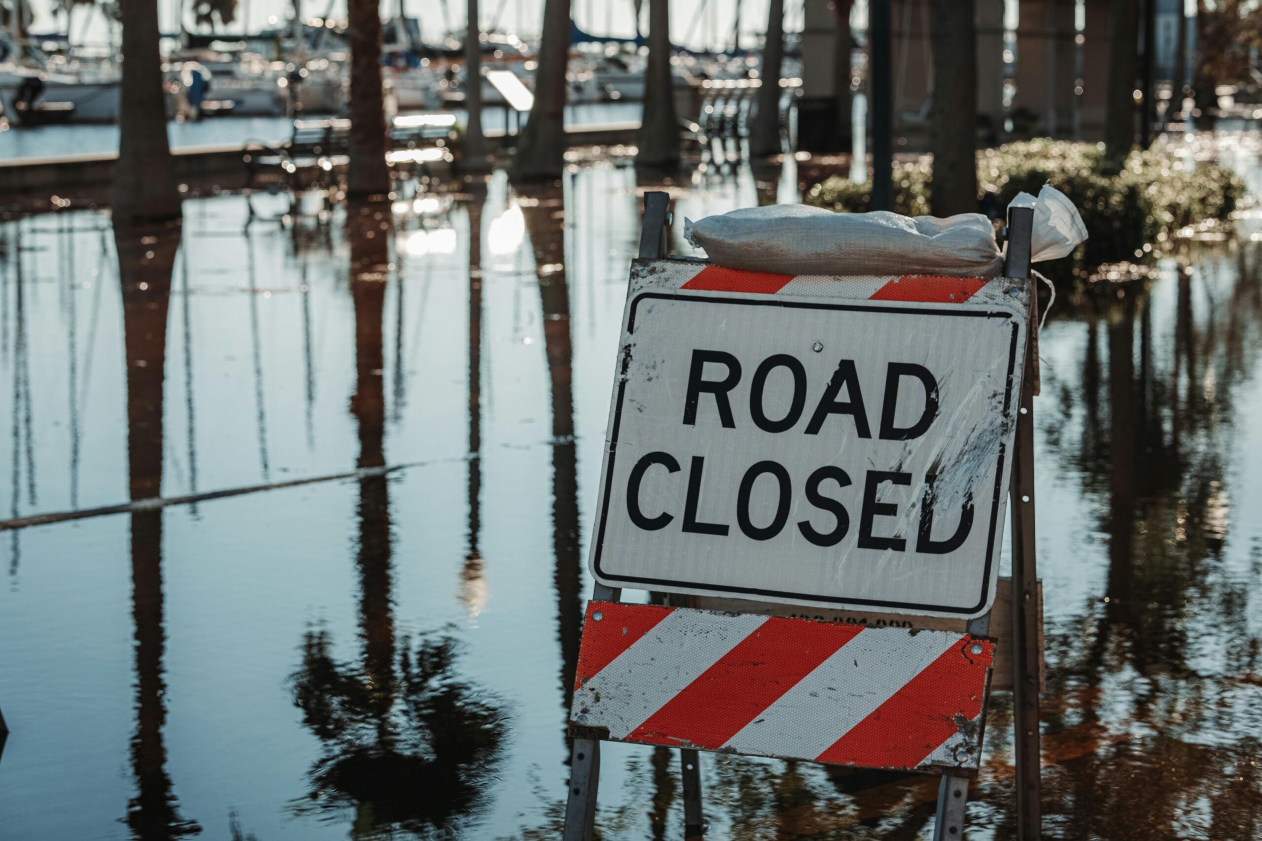 A road closed sign next to a flooded road.