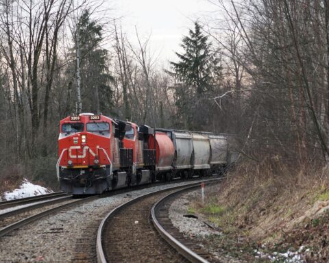 A Canadian National Railway locomotive on a railroad track between woodsy areas on either side.