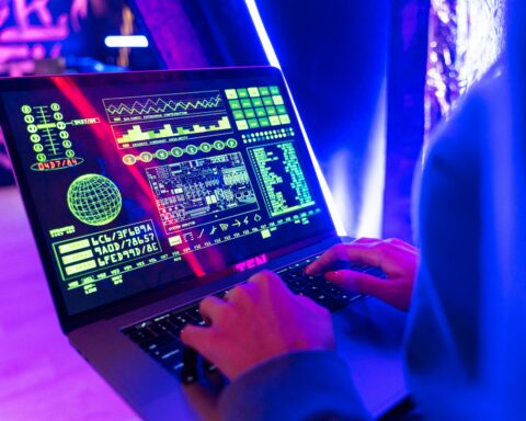 A person uses a computer with various online tools on-screen with neon blue and purple lighting.