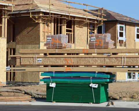 Several houses are being built near a trash bin and additional wood pallets.