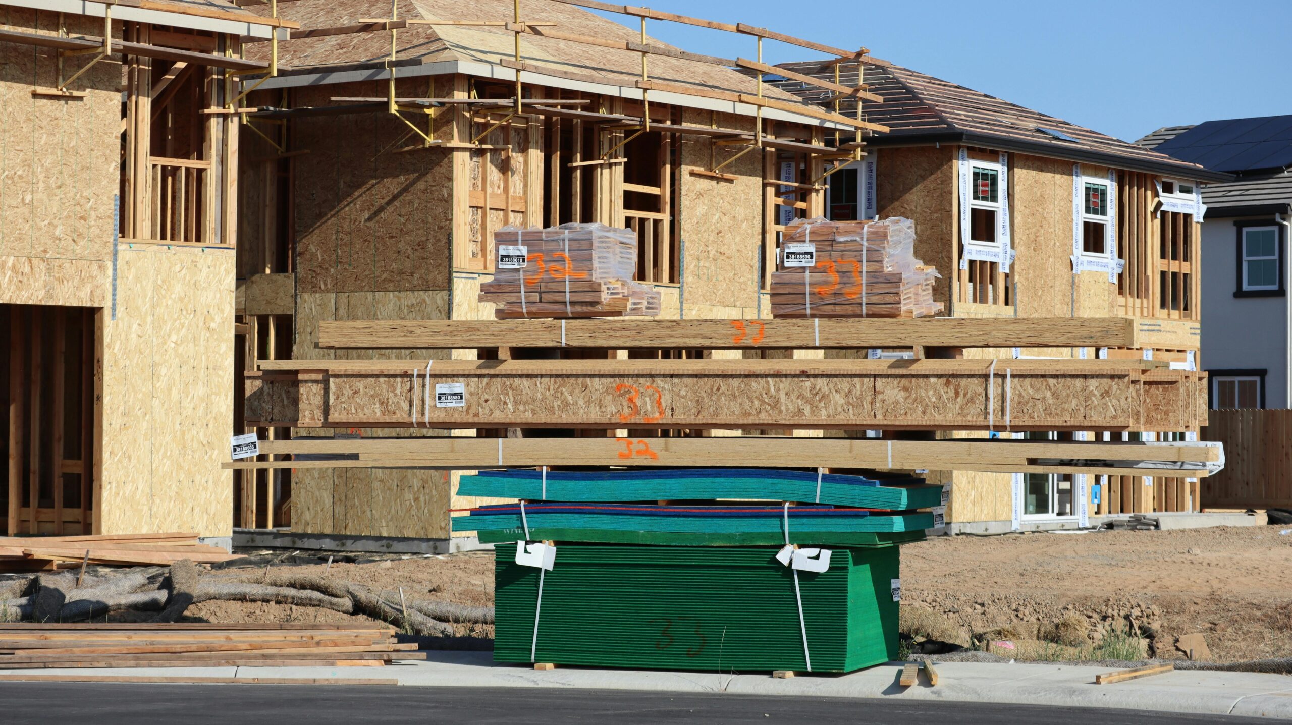 Several houses are being built near a trash bin and additional wood pallets.