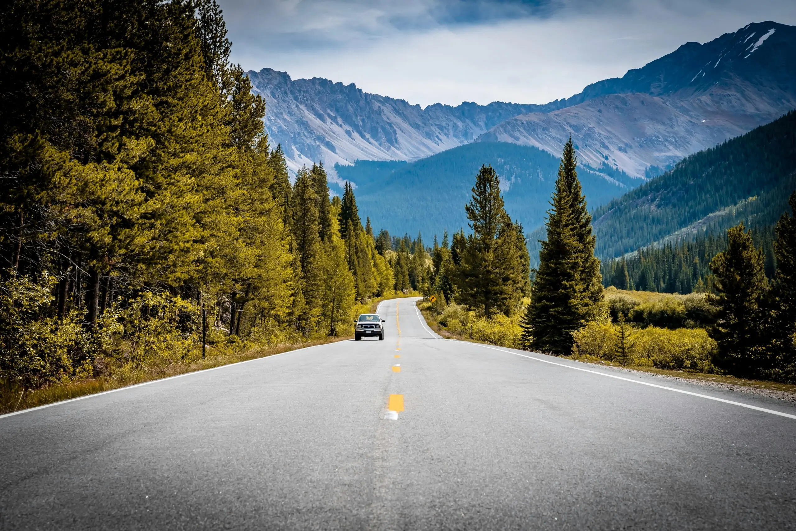 A car in the middle of a scenic Colorado road in the Rocky Mountains.