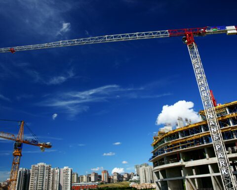 A construction crane looms above a construction site under a blue sky.